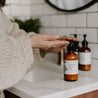 8oz Mount Bachelor Body Lotion on a bathroom countertop being dispensed in to a woman's hands. 