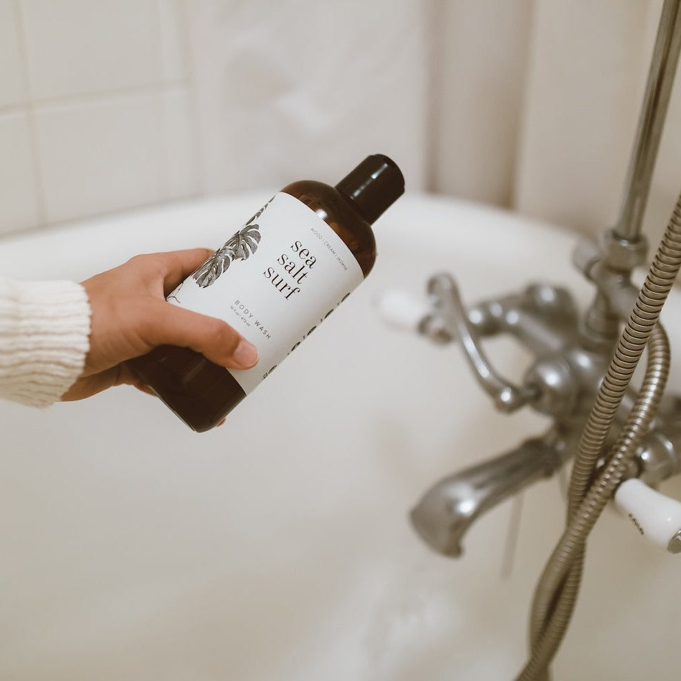 16oz Sea Salt Surf Body Wash being held over a bathtub. 