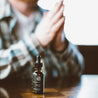 1oz Tobacco Teak Beard Oil on a table with a man in the background. 