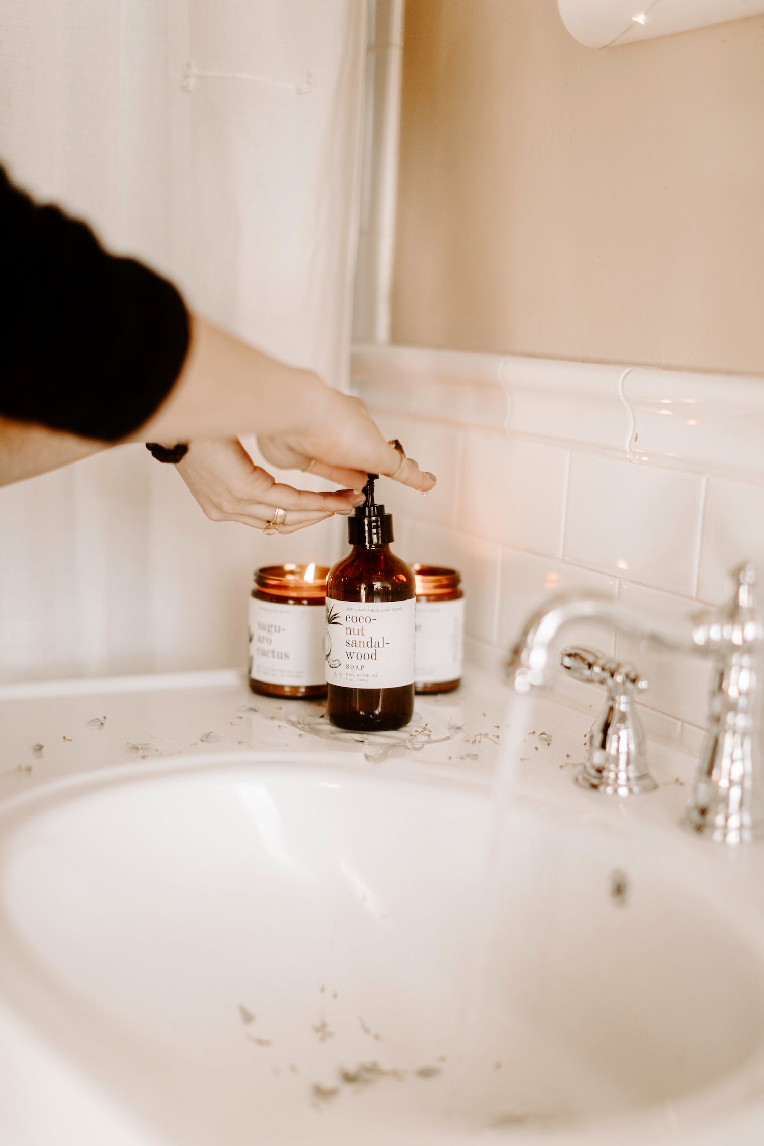 8oz Coconut Sandalwood Liquid Soap on a bathroom countertop being dispensed into hands.