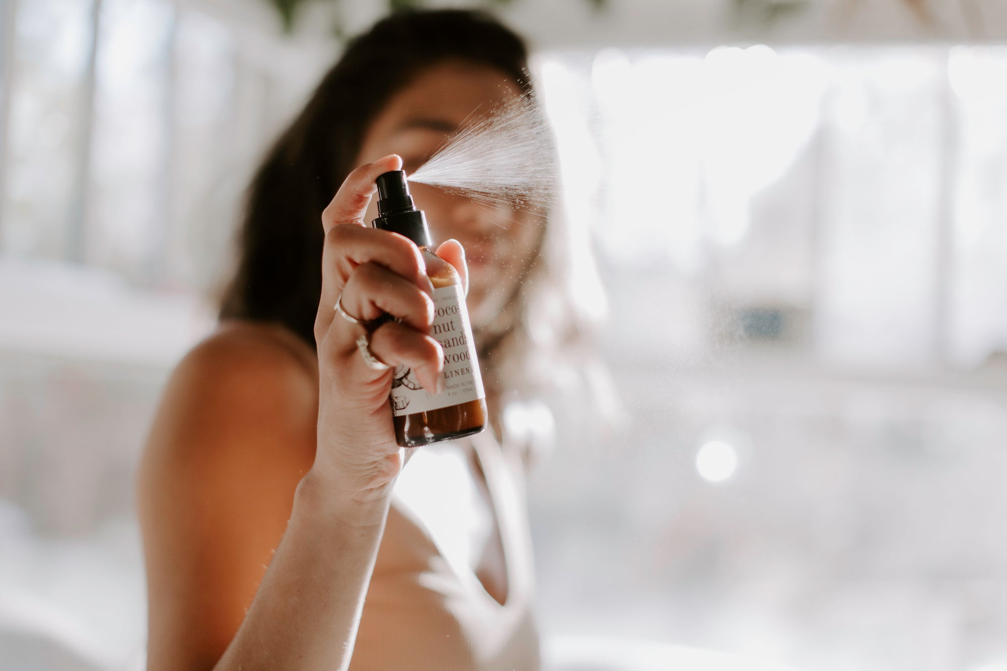 4oz Coconut Sandalwood Linen Spray being sprayed by a woman. 