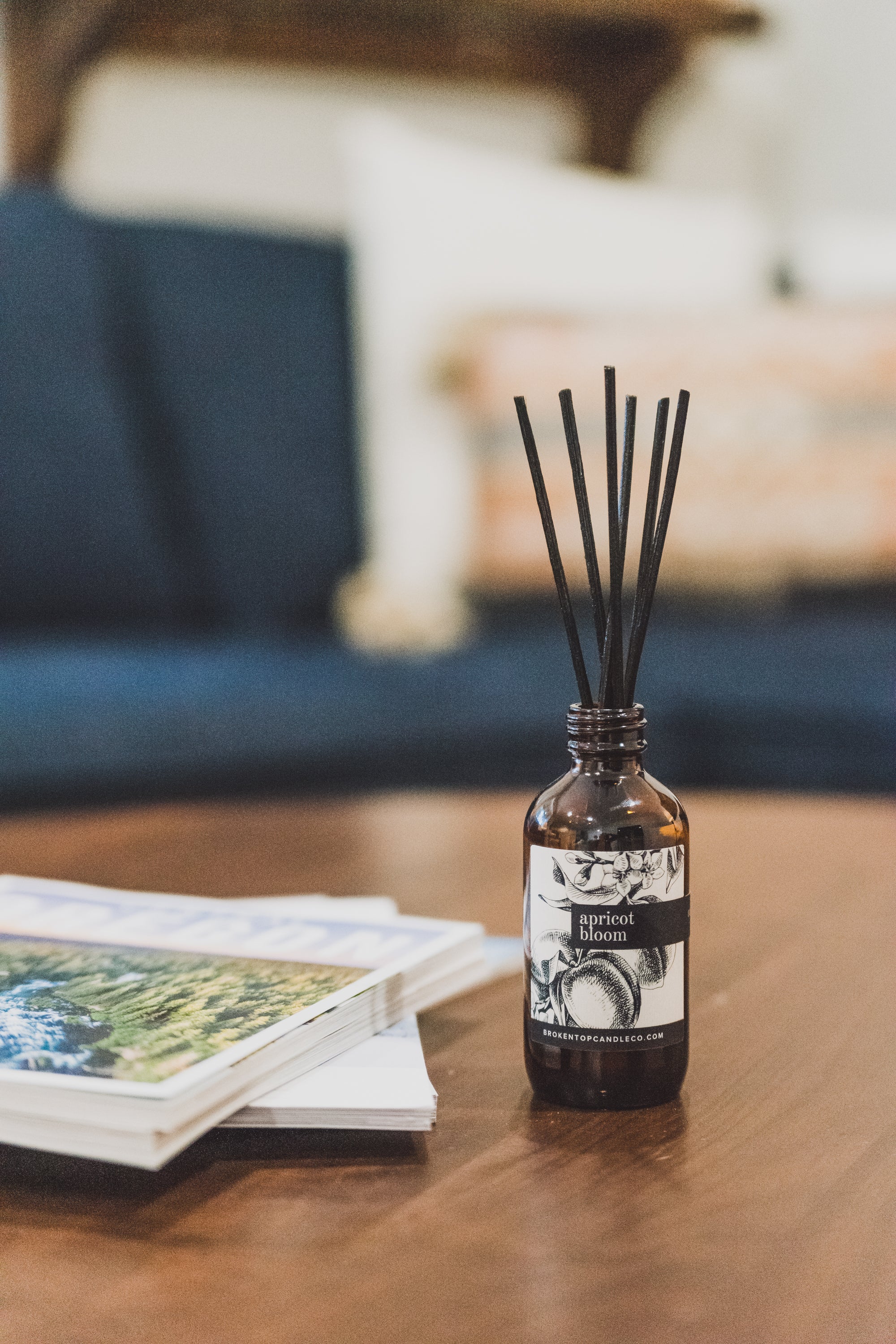 Apricot Bloom Reed Diffuser on a coffee table next to a stack of magazines. 