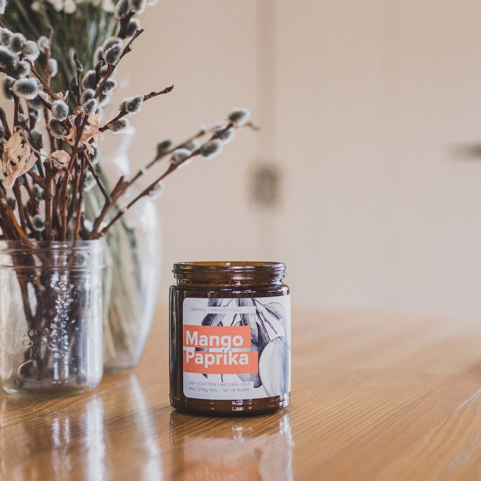 9oz Mango Paprika Soy Candle on a wooden table. 