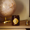 9oz Buttered Rum Soy Candle on wooden table next to a globe and a gold candle snuffer. 