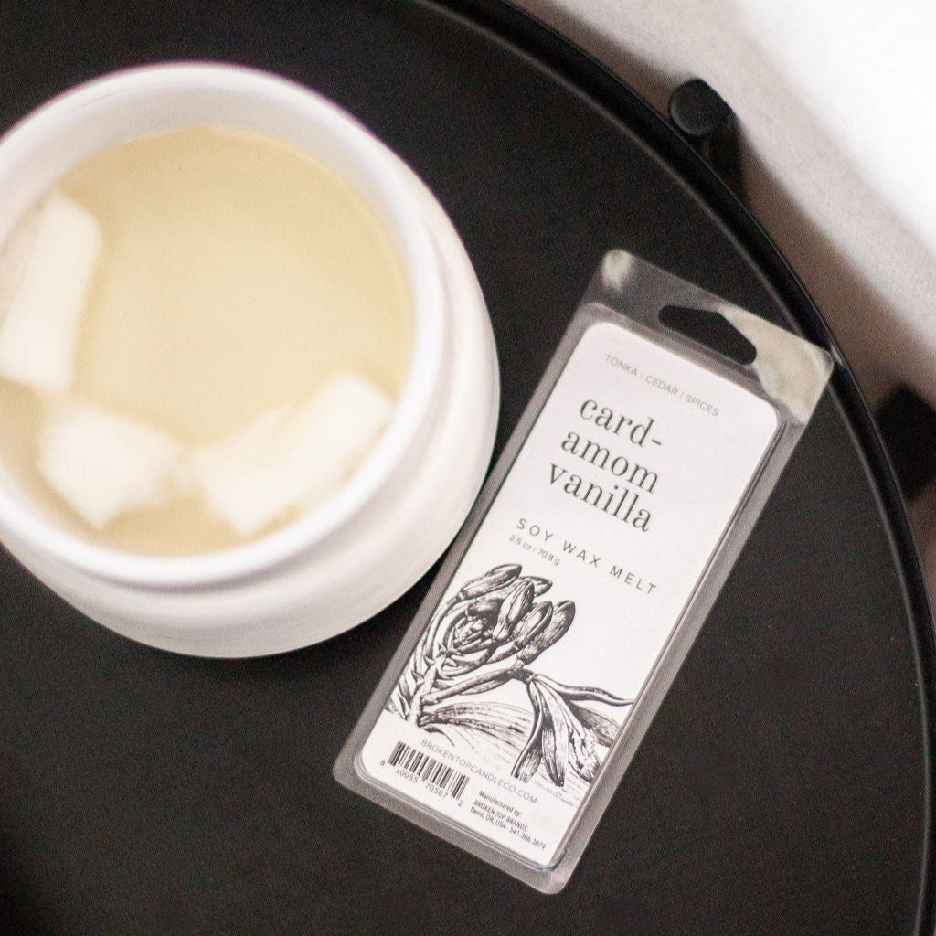 Cardamom Vanilla Soy Wax Melt on black side table next to a white wax melter. 