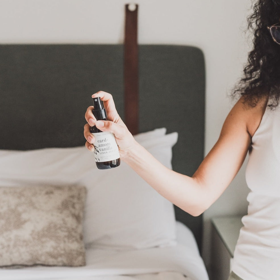 4oz Cardamom Vanilla Linen Spray being sprayed by a woman. 