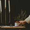 9oz Christmas Tree Soy Candle being positioned by a hand on a wooden table next to Christmas decor. 