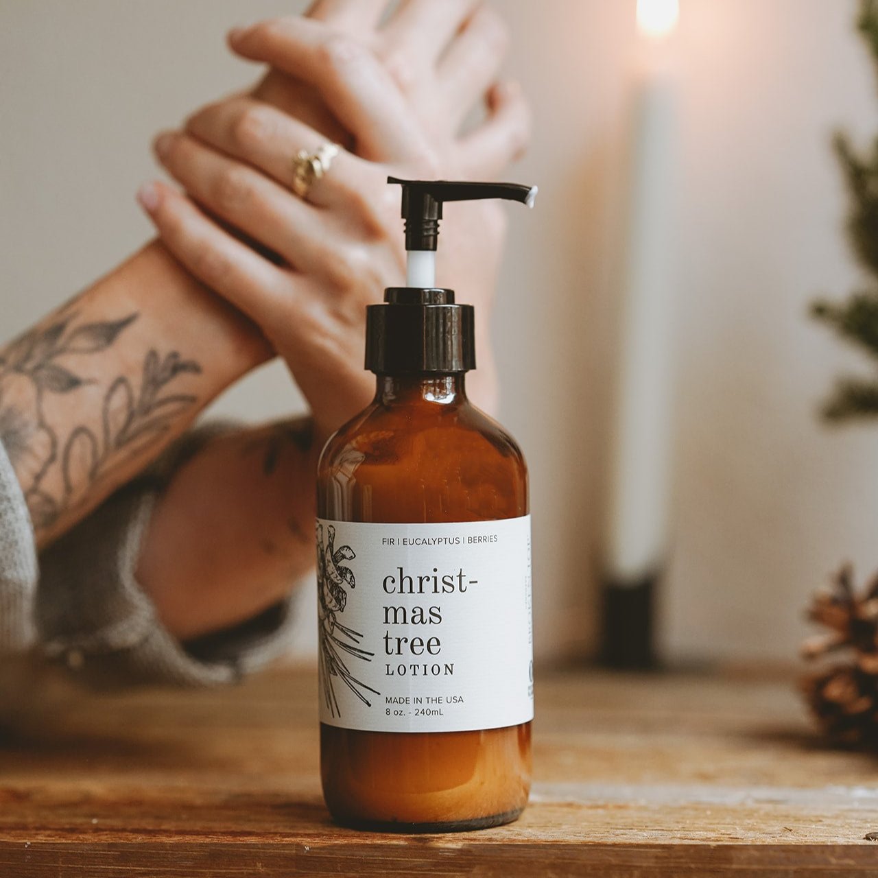 8oz Christmas Tree Body Lotion on wooden table with hands in the background. 