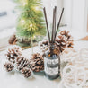 Christmas Tree Reed Diffuser on a table surrounded by pine cones and Christmas decor. 