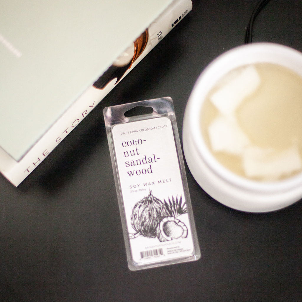 Coconut Sandalwood Soy Wax Melt on black side table text to a white wax melter and books. 