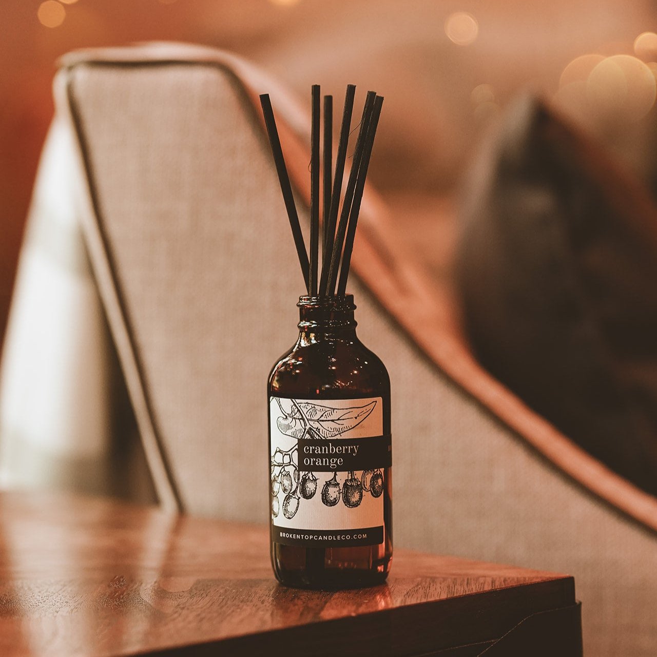 Cranberry Orange Reed Diffuser on wooden side table. 