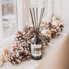 Cranberry Orange Reed Diffuser on window sill next to pine cones and small disco balls. 