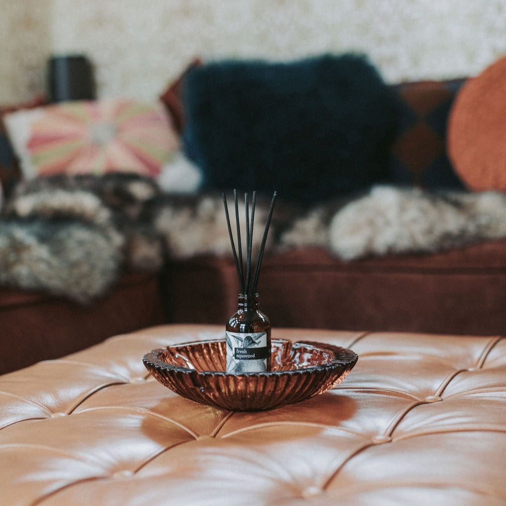 Fresh Squeezed Reed Diffuser in glass bowl on a leather ottoman. 