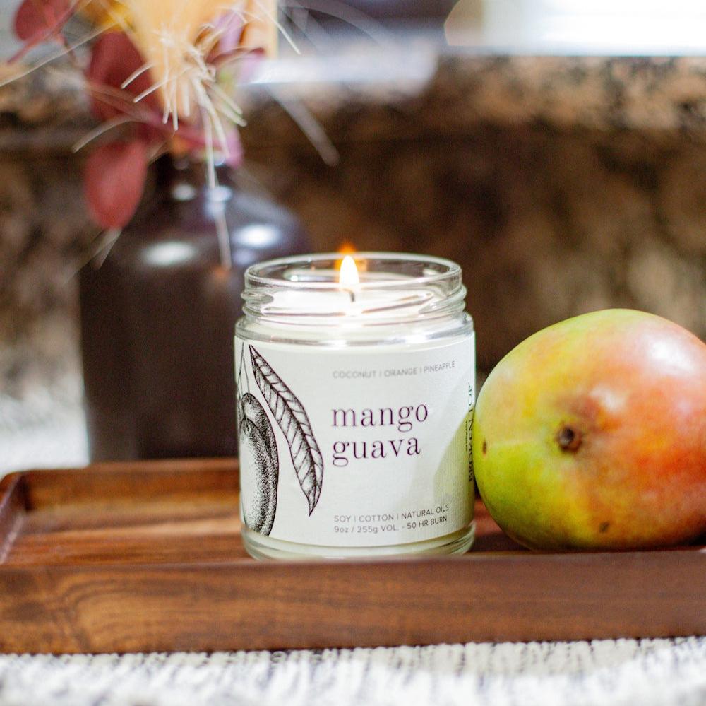 9oz Mango Guava Soy Candle on a wooden try next to a mango. 