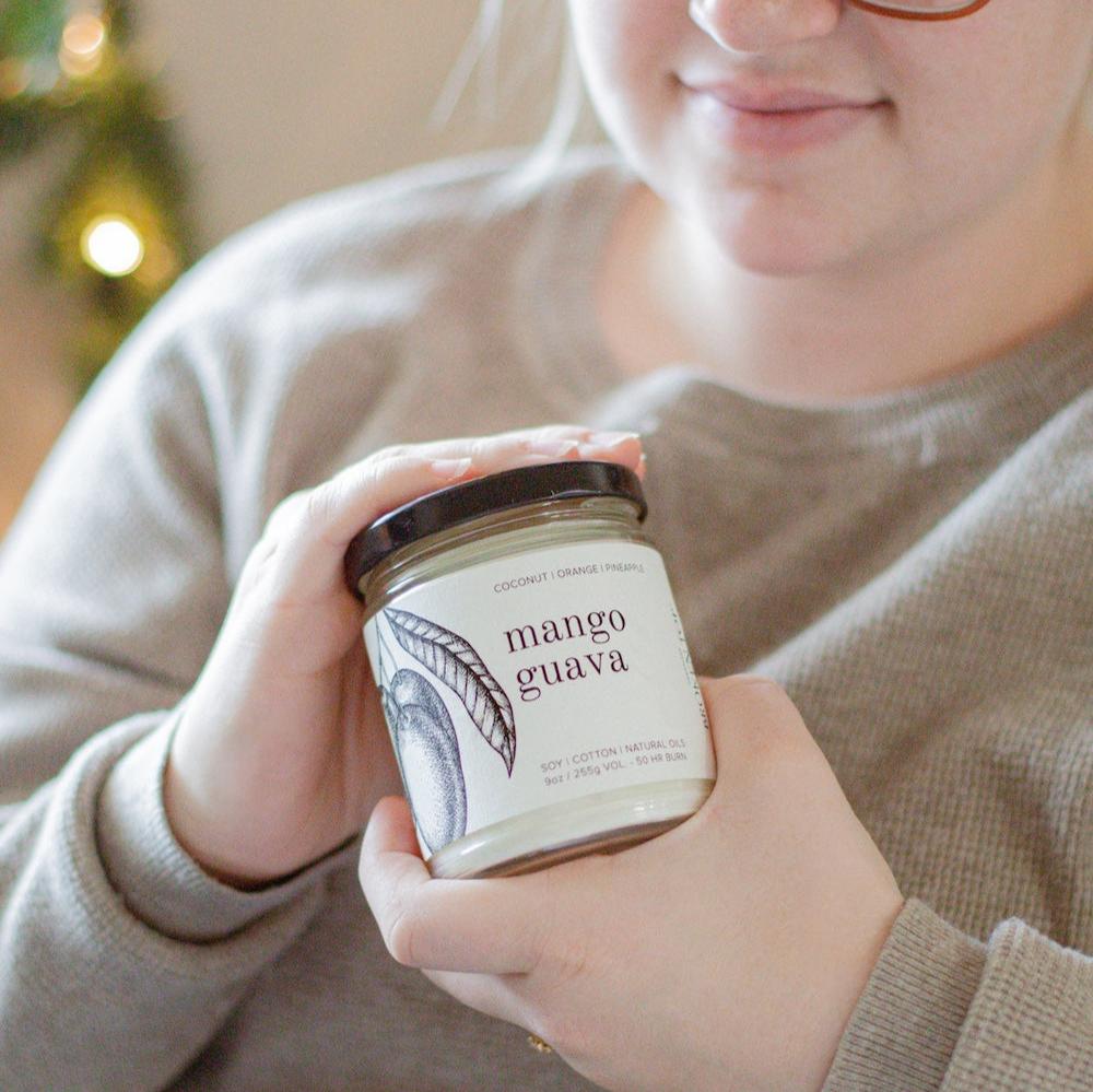 9oz Mango Guava Soy Candle being held by a young woman. 