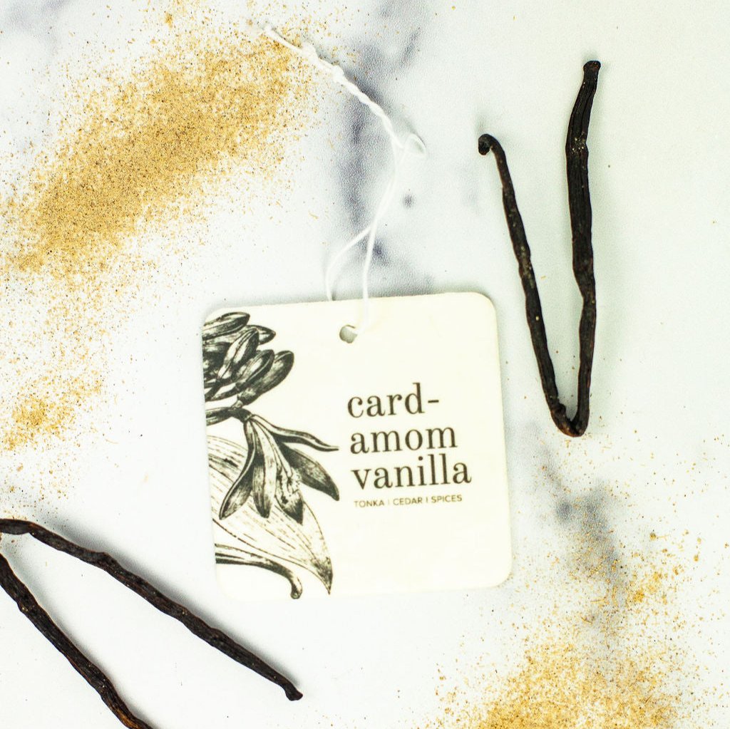 Cardamom Vanilla Car Freshener on marble countertop next to vanilla beans and spices. 