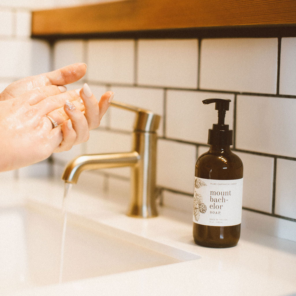 8oz Mount Bachelor Liquid Soap on a bathroom sink countertop with hands washing in the background. 