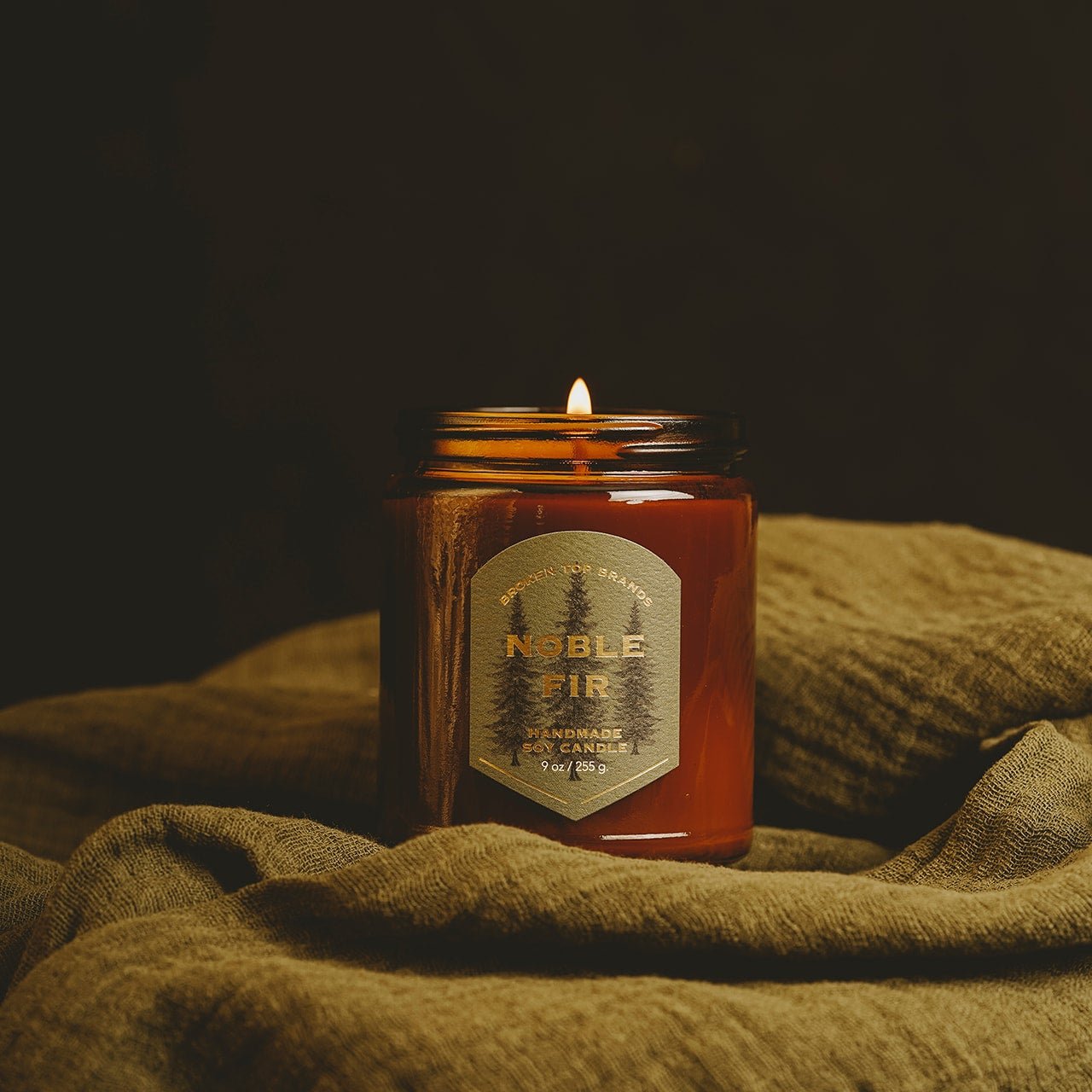 9oz Noble Fir Soy Candle on draped green fabric. 