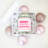 'Merry Pinkmas' 9oz Soy Candle in a gift box surrounded by pink Christmas tree ornaments. 