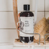 16oz Sea Salt Surf Body Wash in a shower caddy next to a luffa. 