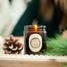 9oz Yule Log Soy Candle on a decorative wooden tray next to a pine cone and pine needles. 