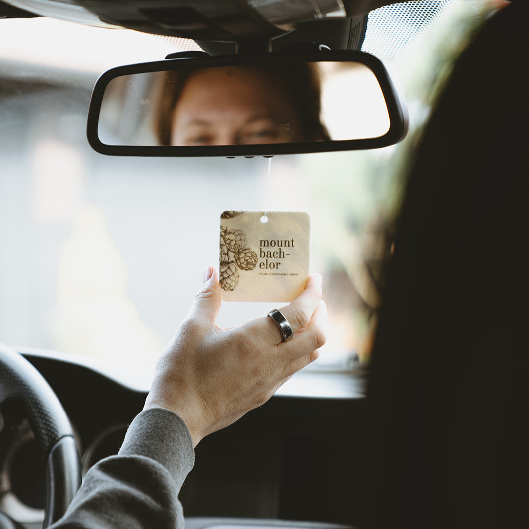 Mount Bachelor Car Freshener being adjusted by a hand on a rear view mirror. 