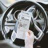 Mount Bachelor Car Freshener being held in front of a car steering wheel. 