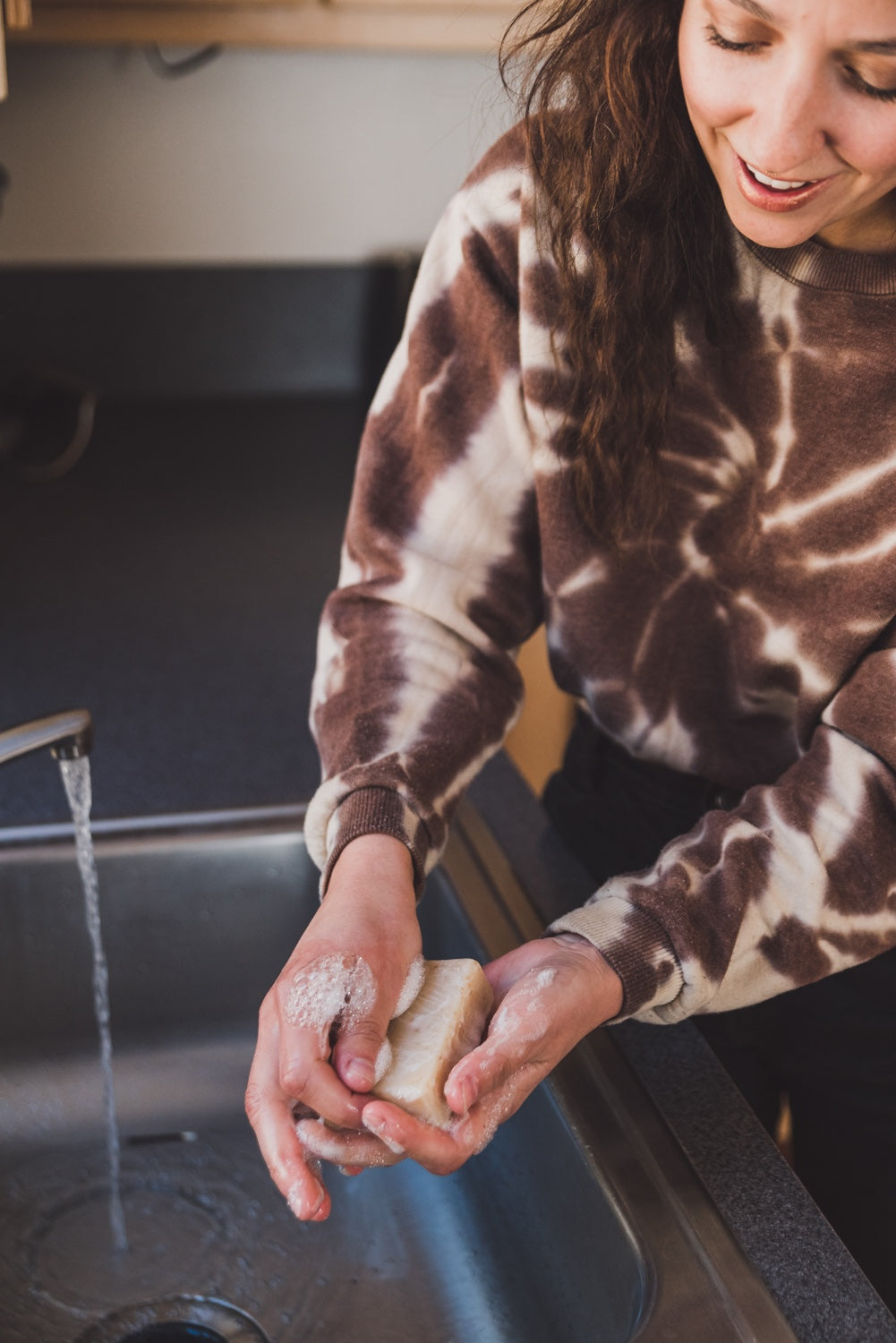 Woman lathering a bar of soap in a kitchen sink. 